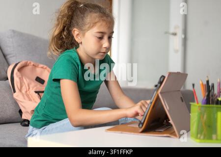 Bambina delle elementari concentrata sul suo tablet mentre studia a casa. Foto Stock