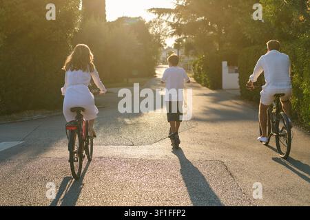 Ciclismo e pattinaggio in famiglia al tramonto in una tranquilla strada residenziale Foto Stock
