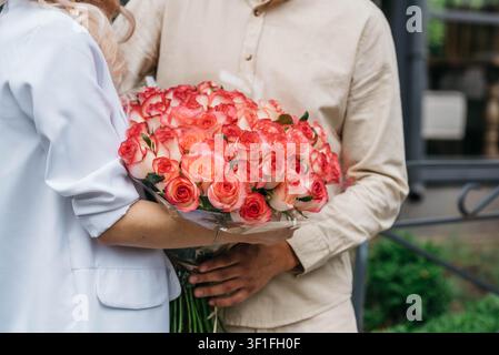 Una coppia innamorata che tiene un lussuoso mazzo di rose rosa fresche. Regalo floreale elegante che simboleggia romanticismo, amore, anniversario, matrimonio, San Valentino, apprezzamento e celebrazioni speciali. Primo piano con luce naturale soffusa e messa a fuoco selettiva. Foto Stock