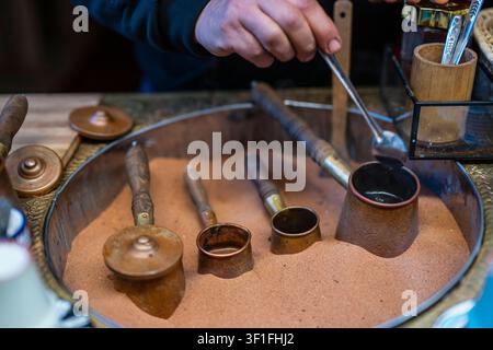 Uomo che prepara un caffè turco tradizionale nella sabbia calda Foto Stock