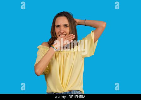 Donna che si sente stressata e pentita, si copre la bocca con la mano su sfondo blu Foto Stock