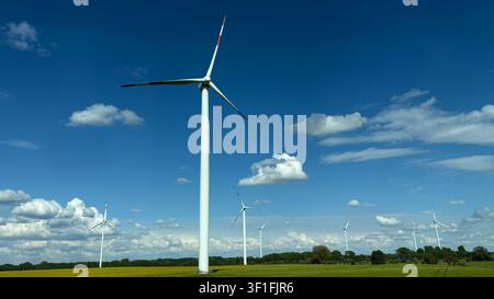 Turbine eoliche che si ergono alte in un campo verde sotto un cielo blu brillante con nuvole sparse Foto Stock