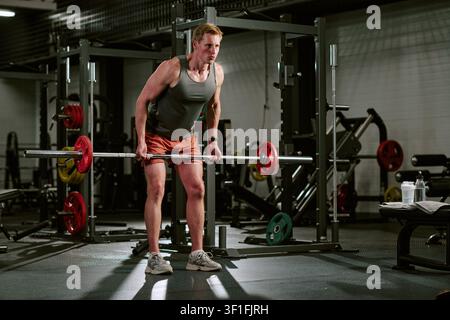 Uomo che solleva un bilanciere durante l'allenamento di forza in palestra Foto Stock