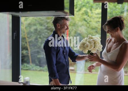 Un uomo regala un mazzo di rose bianche a una donna sorridente Foto Stock