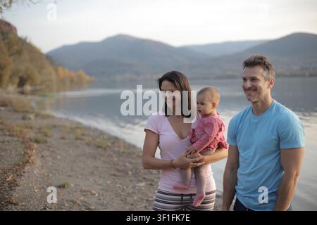 Famiglia felice di tre persone che godono della natura presso un lago Foto Stock