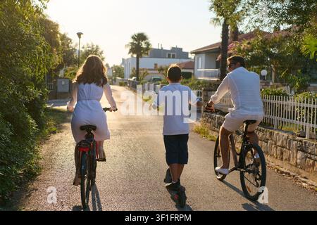 Famiglia in bicicletta insieme su una strada di periferia soleggiata durante la passeggiata mattutina delle vacanze estive Foto Stock