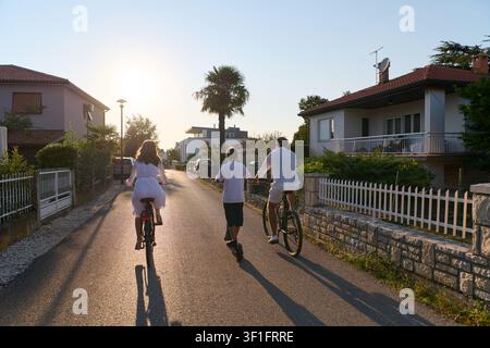 Famiglia in bicicletta insieme al tramonto su una tranquilla strada residenziale vicino a Umag Foto Stock