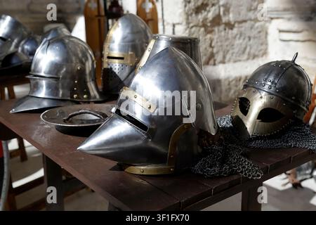 Collezione di elmi medievali in metallo esposti su un tavolo di legno in un ambiente storico. Foto Stock