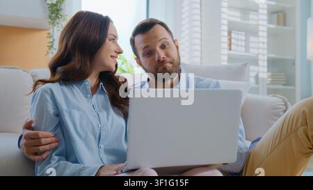 Famiglia caucasica felice che guarda il laptop, abbracciandosi, coccolandosi, parlando, scegliendo beni e-commerce, facendo acquisti su internet insieme, uomo e donna che si abbracciano, parlano Foto Stock