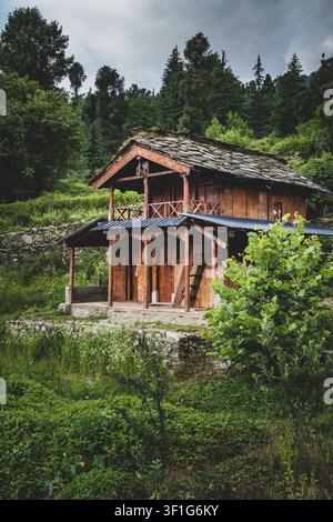27 giugno 2026, Uttarakhand India.. Capanna di legno rustica su una collina verde circondata dalla foresta sotto un cielo nuvoloso, casa di campagna tranquilla con natura Foto Stock