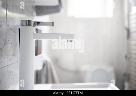 Un piano prospettico ravvicinato che mostra piastrelle di ceramica lucide con un motivo a trama marmo grigio e giunti bianchi in un piccolo bagno luminoso. Foto Stock