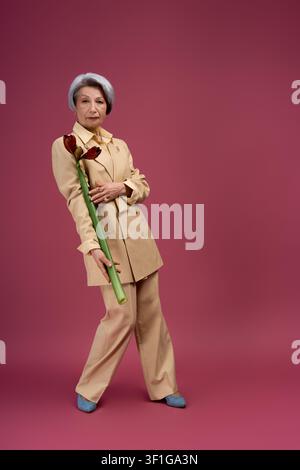 Bella donna anziana vestita con abiti alla moda posa con grazia tenendo un fiore Foto Stock
