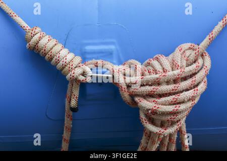 Una corda da arrampicata arrotolata legata a un moschettone di metallo attaccato a una superficie gonfiabile blu, fibre strutturate e fili traccianti rossi visibili, funzionale per esterni Foto Stock