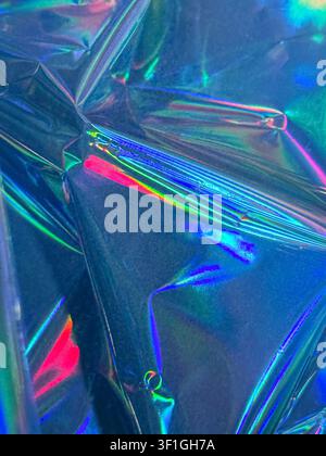 Scatto in studio a distanza ravvicinata, vista astratta di una lamina metallica olografica accartocciata. Superficie strutturata con riflessi di luce iridescenti vivaci in rosa, blu, an Foto Stock