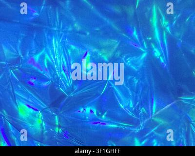 Tessuto di cellophane blu metallico accartocciato che riflette la luce con vivaci riflessi iridescenti acquamarina e viola. Foto in primo piano in studio che mette in mostra la trama Foto Stock