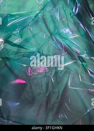 Prima di un materiale in cellophane verde che mostra superfici riflettenti e pieghe profonde. Sottili riflessi rosa aggiungono tocchi di colore astratti. Ideale per packaging Foto Stock