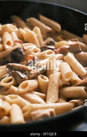 pasta cremosa ai funghi preparata in una padella rustica in ghisa nera. Il piatto presenta penne perfettamente cotte ricoperte da una salsa ricca Foto Stock