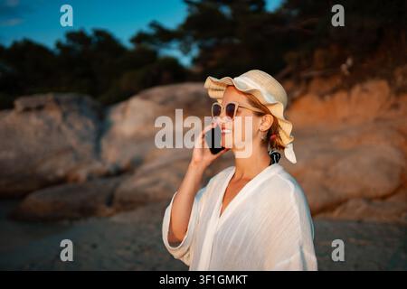 Donna che parla al smartphone e si gode le vacanze al tramonto sulla spiaggia Foto Stock