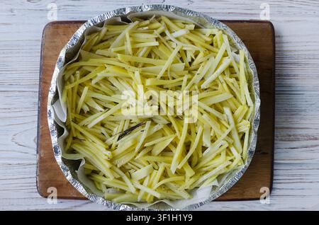 Patate tagliate a striscioline in una teglia da forno con aglio, rosmarino e sale su una superficie di legno chiara. Piatto tradizionale svizzero röschti. Vista dall'alto. Orizzontale Foto Stock