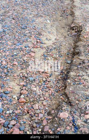 Struttura ruvida di ghiaia e sabbia. Sfondo naturale di un sentiero di terreno eroso con piccoli ciottoli di granito rosa, pietre frantumate e dettagli di pista sterrata ou Foto Stock