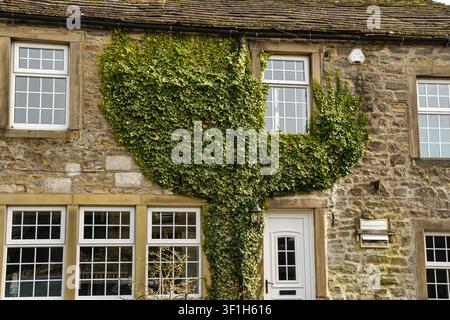 Casa in pietra tradizionale con facciata ricoperta di edera nella campagna dello Yorkshire, Inghilterra. Architettura storica del villaggio inglese con pareti in pietra naturale Foto Stock