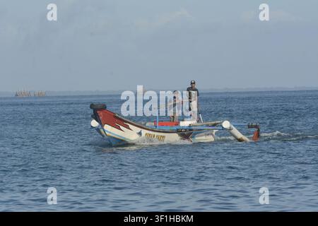 Pescatori tradizionali indonesiani che operano un piccolo peschereccio a motore con bilanciere in legno etichettato Sinar Sakti sulle acque blu dell'oceano a Ujung Kulon Foto Stock