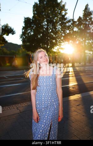 Ritratto di moda di una donna bionda sorridente all'aperto all'ora dorata con bagliore solare, abbigliamento estivo elegante e stile di vita urbano. Foto Stock