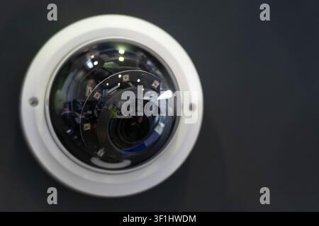 Primo piano di una telecamera a cupola con sistema di videosorveglianza sotto una copertura protettiva trasparente, montata su un pannello di visualizzazione scuro. Foto Stock