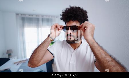 Uomo con capelli ricci che regola gli occhiali da sole, un look alla moda urbano Foto Stock