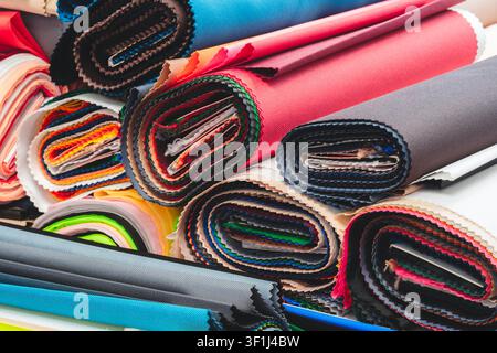Vista ravvicinata di rotoli di tessuto ordinatamente impilati. Colori vivaci e motivi vari riempiono il fotogramma. Le trame includono superfici lisce e a righe. Ideale f Foto Stock