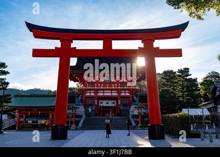 Una donna in piedi all'interno della cornice del Grande Torii Rosso all'ingresso del Santuario di Fushimi Inari Taisha a Kyoto mentre il sole tramonta dietro di lei Foto Stock