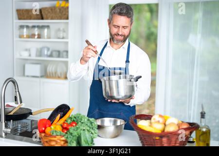 Lo chef di cucina prepara cibo sano. La cucina utilizza verdure colorate. L'uomo gode della cucina casalinga in cucina. Lo chef di cucina, un cuoco, taglia i peperoni Foto Stock