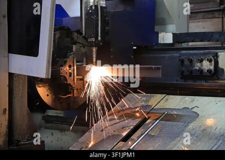 L'immagine mostra attrezzature di taglio laser CNC che tagliano con precisione profili metallici perforati, con scintille ad alta temperatura che esplodono e schizzano. La prec Foto Stock