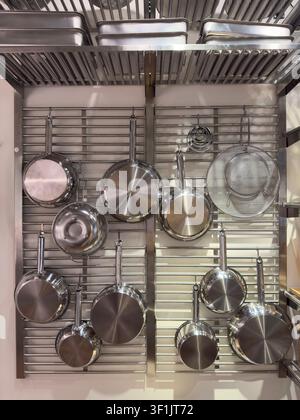 Pentole professionali in acciaio inossidabile appese a una mensola moderna da parete in cucina Foto Stock
