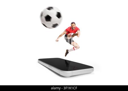 Giocatore di calcio che salta fuori dallo schermo di uno smartphone e calcia un pallone Foto Stock