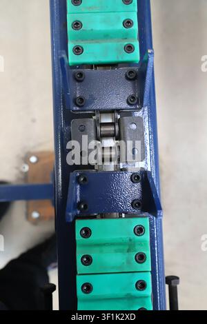 L'immagine è un primo piano di un fissaggio metallico di precisione per macchinari industriali. Il corpo principale è composto da una base metallica blu con resistenza all'usura verde Foto Stock