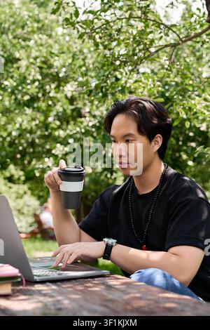 Freelancer si gode il lavoro remoto sotto alberi verdi sorseggiando caffè in estate Foto Stock