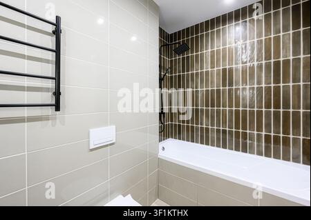 bagno moderno con piastrelle grigio chiaro, un soffione doccia nero e una vasca da bagno bianca. Design pulito e contemporaneo Foto Stock