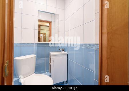 piccolo bagno con piastrelle blu e bianche, un WC, un piccolo mobiletto per il lavandino e uno specchio, incorniciato da porte di legno Foto Stock