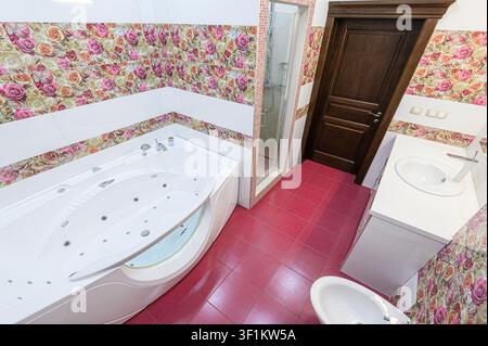 Bagno vivace con vasca idromassaggio, piastrelle a motivi di rose, doccia e porta in legno scuro. Il pavimento è in piastrelle rosa audaci Foto Stock