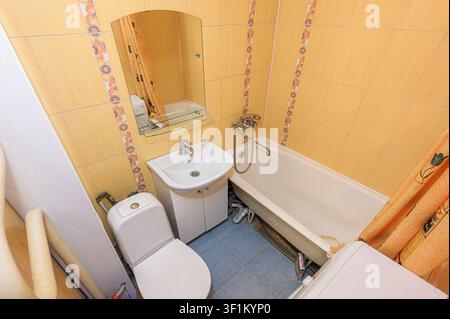 Bagno accogliente con piastrelle gialle, un lavandino bianco, toilette e vasca da bagno. Una tenda da doccia e uno specchio aggiungono dettagli allo spazio compatto Foto Stock