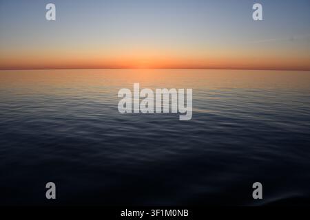 Tramonto arancione che risplende sopra un mare calmo con lievi increspature e spazio copia aperto Foto Stock