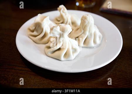 Set di khinkali georgiani tradizionali con ripieno di carne di manzo e maiale saporito, funghi, pollo e formaggio, brodo caldo all'interno servito su w Foto Stock