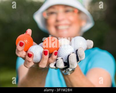 Ritratto ravvicinato di una golfista anziana che tiene più palline da golf tra le mani Foto Stock
