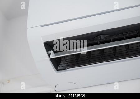 Un primo piano ad angolo basso che si concentra sulla presa d'aria orizzontale aperta e sulle lamelle d'aria interne in plastica di un moderno condizionatore split senza condotto bianco Foto Stock