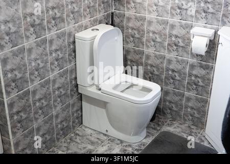 Un primo piano, ripreso da un angolo elevato, di un gabinetto in ceramica bianca pulito con il coperchio aperto, posizionato in un angolo del bagno con marmo grigio abbinato Foto Stock