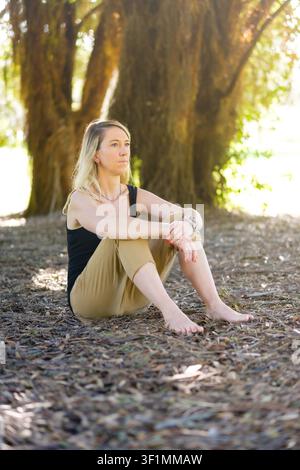 Donna seduta a piedi nudi su foglie secche, che trova pace e consapevolezza nella natura Foto Stock