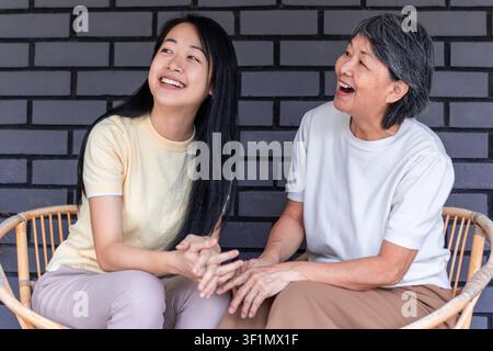 Una gioiosa madre e figlia asiatica condividono un momento felice sedute su sedie all'aperto, esprimendo amore e unità. I loro sorrisi riflettono una profonda fami Foto Stock