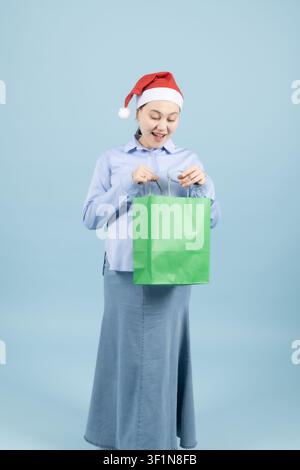 Donna incinta felice con cappello di Babbo Natale e borsa della spesa verde Foto Stock