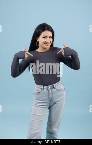 Giovane donna forte che mostra i suoi muscoli con un sorriso sicuro di sé in studio Foto Stock